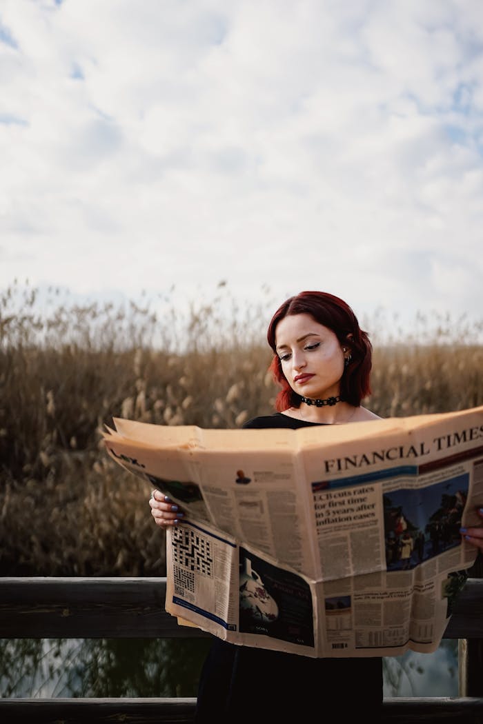 A red-haired woman reads the Financial Times in a natural outdoor setting.